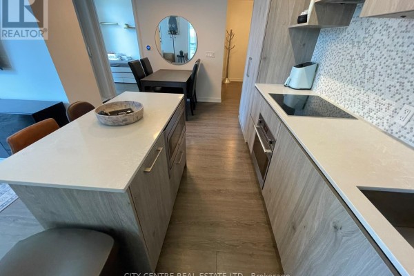 View of kitchen counter, sink, stovetop, and dining area with round mirror. - 1602 - 1 Yorkville Avenue, Toronto