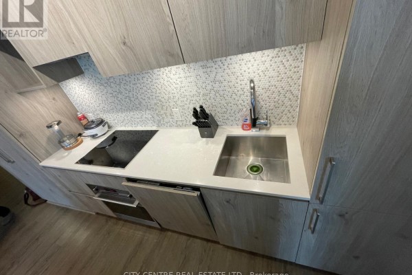 Close-up of kitchen sink, faucet, and stovetop with mosaic tile backsplash. - 1602 - 1 Yorkville Avenue, Toronto