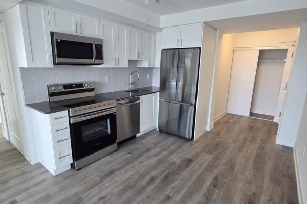 White kitchen cabinets, stainless steel appliances, and gray wood-look flooring. - 1602 - 1010 Sandy Beach Road, Pickering