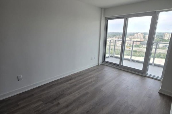Empty room with white walls, gray wood-look flooring, and balcony access. - 1602 - 1010 Sandy Beach Road, Pickering