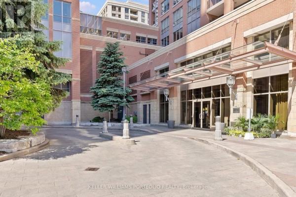 Driveway leading to the brick building entrance with a glass awning and trees. - 1602 - 4090 Living Arts Drive, Mississauga