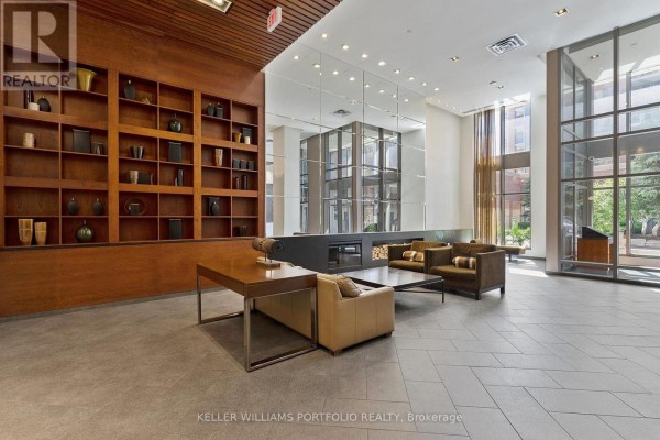 Building lobby with a large wooden shelved wall, modern fireplace, and seating areas. - 1602 - 4090 Living Arts Drive, Mississauga