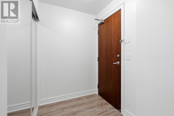 Apartment entrance hallway with a wooden door, mirrored closet, and light walls. - 1602 - 4090 Living Arts Drive, Mississauga