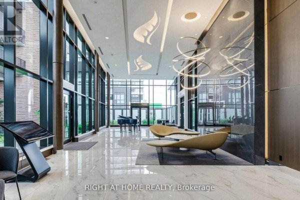 Spacious building lobby with marble floors, modern seating, a grand piano, and large windows. - 1602 - 95 Mcmahon Drive, Toronto