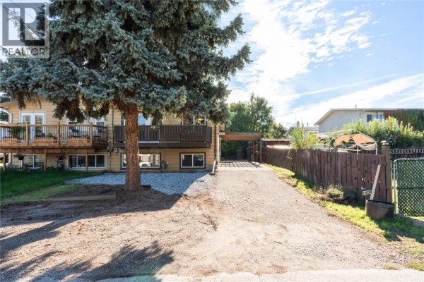Front view of a beige duplex with a wooden deck and covered carport. - 1603b 45th Street, Vernon
