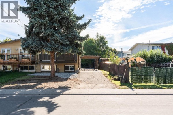 Side exterior of a duplex showing a driveway, wooden fence, and greenhouse. - 1603b 45th Street, Vernon