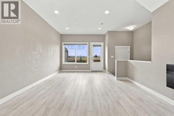 Living area with light wood floors, grey walls, and a large window with exterior view. - 1604, 32 Horseshoe Crescent, Cochrane
