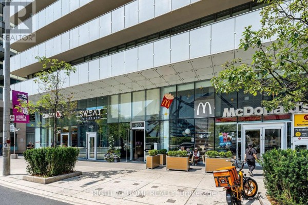 Street level view of the building entrance with planters and outdoor seating. - 1604 - 200 Bloor Street W, Toronto