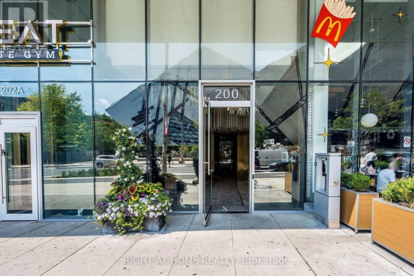 Close-up of the building's main entrance with glass doors and adjacent storefronts. - 1604 - 200 Bloor Street W, Toronto