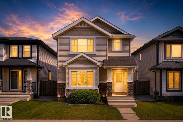 Front exterior of a two-story home with light beige siding and stone accents. - 16040 11 Av Sw, Edmonton