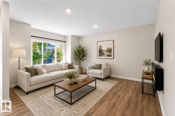 Living room with a large white sofa, armchair, coffee table, and rug. - 16040 11 Av Sw, Edmonton