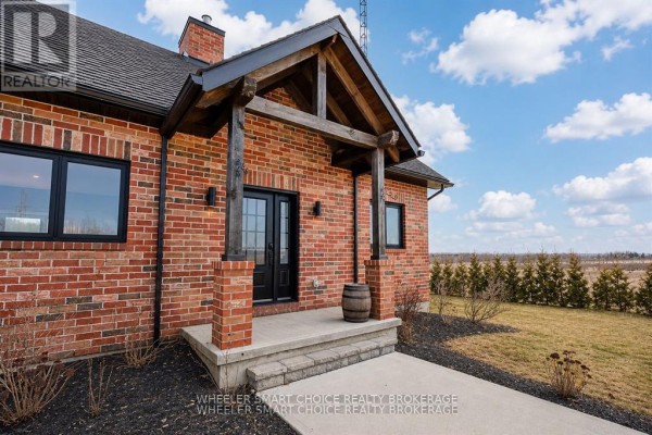 Covered front entrance with a wooden beam support, brick pillars, and a glass double door. - 16040 County Rd 18 Road, South Stormont