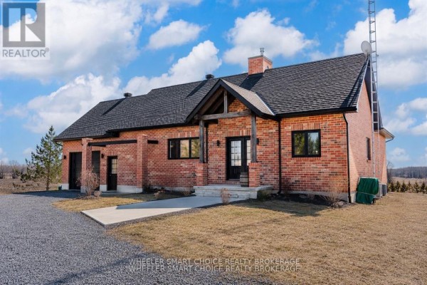 Side view of the red brick house showing a detached garage and a sloped grassy yard. - 16040 County Rd 18 Road, South Stormont