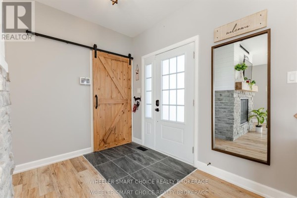Interior view of an entryway with a wooden barn door, white double doors, and a reflection of a fireplace. - 16040 County Rd 18 Road, South Stormont