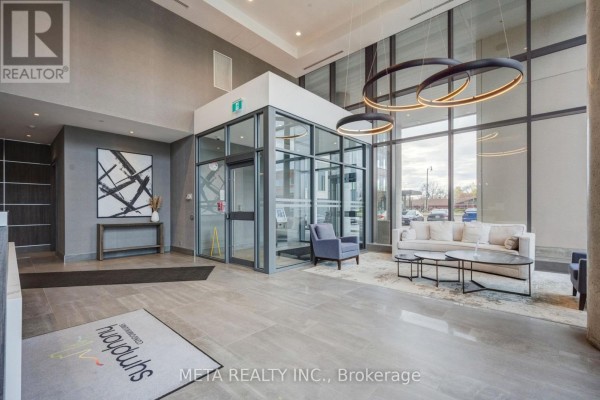 Spacious building lobby with a glass elevator, seating area, and modern lighting. - 1605 - 15 Lynch Street, Brampton