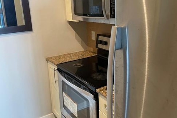 Kitchenette with a stainless steel refrigerator, black stovetop, and granite countertops. - 1605 - 4070 Confederation Parkway W, Mississauga