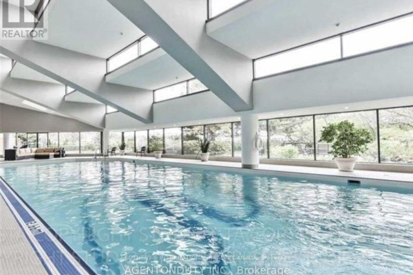 Indoor swimming pool with large windows overlooking trees and lounge furniture. - 1605 - 65 Harbour Square, Toronto