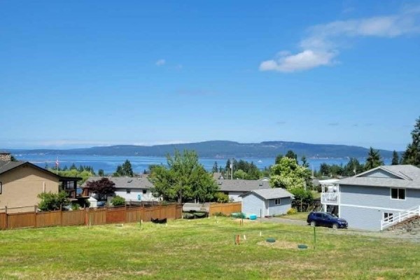 Grassy lot with a light blue house, trees, and houses on a hillside. - 1605 Adelaide St, Crofton