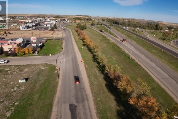 Aerial view looking down a two-lane road lined with trees, with a highway on the right and commercial buildings on the left. - 1605 North Service Road E, Swift Current