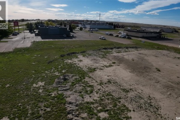 Aerial view of a vacant, partially cleared lot with sparse vegetation and an uneven terrain, with commercial buildings in the distance. - 1605 North Service Road E, Swift Current
