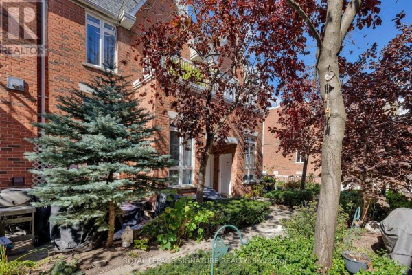 Exterior of a brick townhouse with a front yard garden and mature trees. - 1606 - 12 Sudbury Street, Toronto