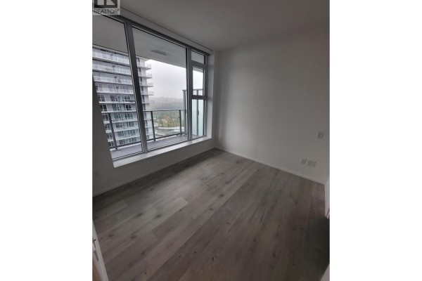 Bedroom with large window overlooking city buildings and green space. - 1606 3809 Evergreen Place, Burnaby