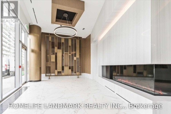 Modern lobby with white marble floors, a linear fireplace, and a decorative wood screen. - 1607 - 15 Queens Quay East Street, Toronto