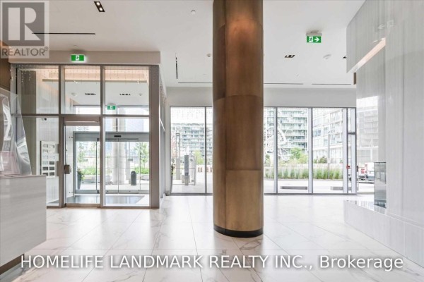 Spacious lobby with large windows, a central wood-clad column, and glass entrances. - 1607 - 15 Queens Quay East Street, Toronto