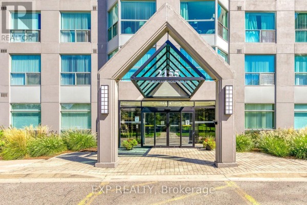 Entrance to the apartment building at 2155 Burnhamthorpe Road with glass doors and a concrete overhang. - 1607 - 2155 Burnhamthorpe Road, Mississauga