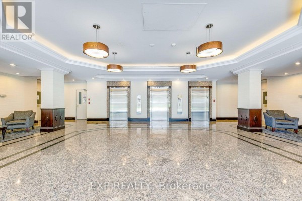 Interior of the apartment building lobby with polished granite floors, three elevators, and decorative lighting. - 1607 - 2155 Burnhamthorpe Road, Mississauga
