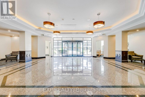 Apartment building lobby with glass doors, seating areas, polished floors, and decorative lighting. - 1607 - 2155 Burnhamthorpe Road, Mississauga