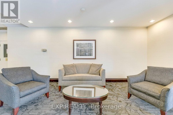 Lobby seating area with two armchairs, a loveseat, a circular coffee table, and artwork on the wall. - 1607 - 2155 Burnhamthorpe Road, Mississauga