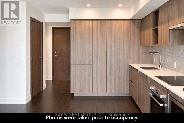 View of the apartment hallway leading to the kitchen area with wood cabinets and stainless steel appliances. - 1608 - 19 Bathurst Street, Toronto