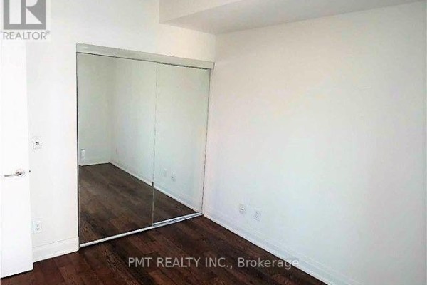 Bedroom with dark wood floors and a large closet with mirrored sliding doors. - 1608 - 80 John Street, Toronto
