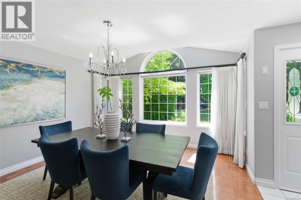 Dining room with dark wood table, blue upholstered chairs, crystal chandelier, and large windows. - 1608 Marina Way, Nanoose Bay