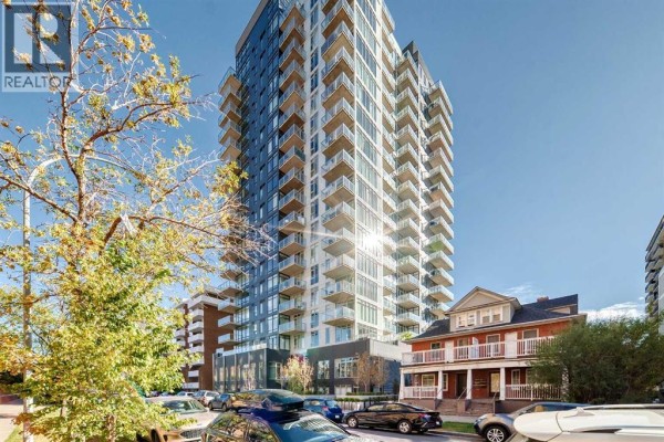 Exterior view of a tall condominium building with balconies and adjacent red brick houses. - 1609, 1319 14 Avenue Sw, Calgary
