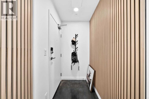 Interior hallway with white walls, a door, a black coat rack, and slatted wood paneling. - 1609, 1319 14 Avenue Sw, Calgary