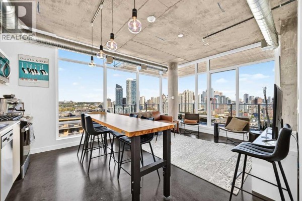 Combined kitchen and dining area with a large wooden table, black chairs, and city skyline views. - 1609, 1319 14 Avenue Sw, Calgary