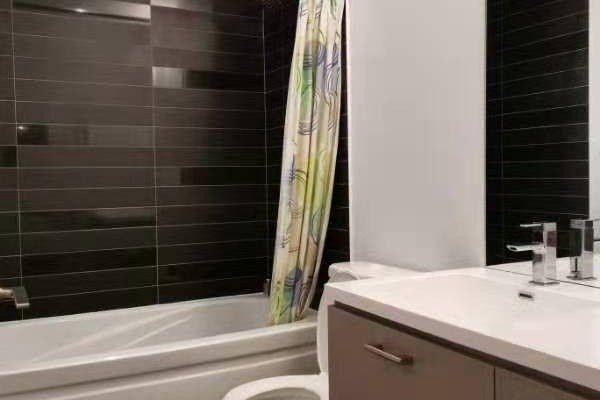 Bathroom with bathtub, shower curtain, white sink, and dark tiled walls. - 1609 - 87 Peter Street, Toronto