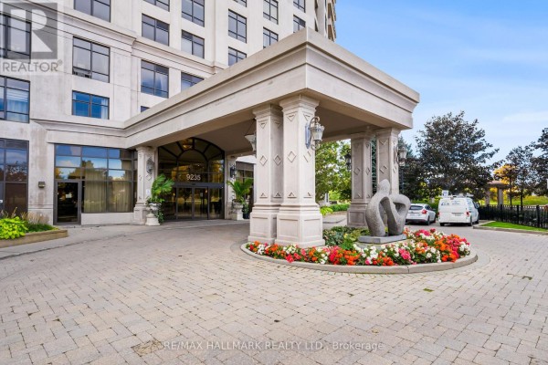 Covered entrance to apartment building with stone pillars and decorative floral arrangements. - 1609 - 9235 Jane Street, Vaughan