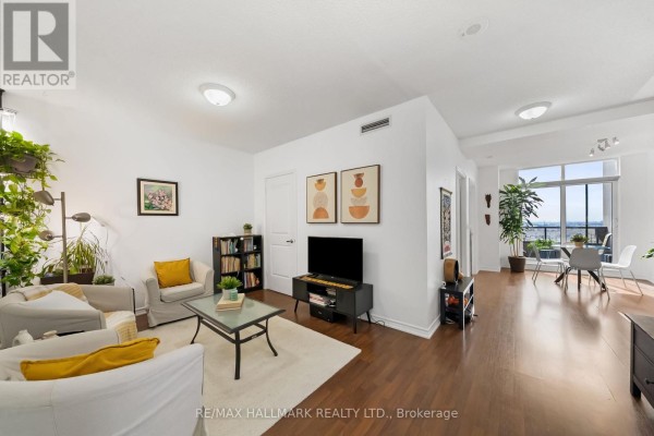 Living room and dining area with white walls, hardwood floors, and large windows overlooking the city. - 1609 - 9235 Jane Street, Vaughan