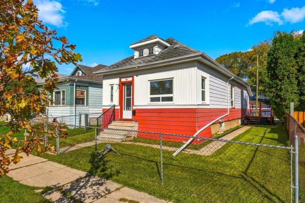 Side view of a small white and red house with a fenced yard and trees. - 161 Atlantic Avenue, Winnipeg