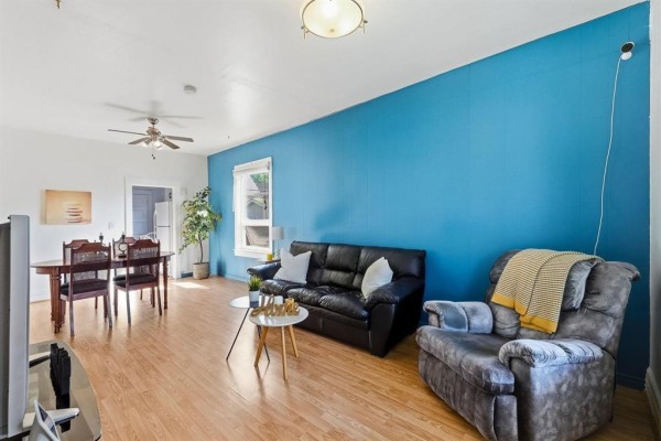 Living room with a blue accent wall, black leather sofa, recliner, and dining area. - 161 Atlantic Avenue, Winnipeg
