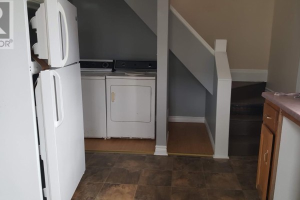 Laundry area with white washer and dryer beside a staircase with dark treads. - 161 Hanover Street, Summerside