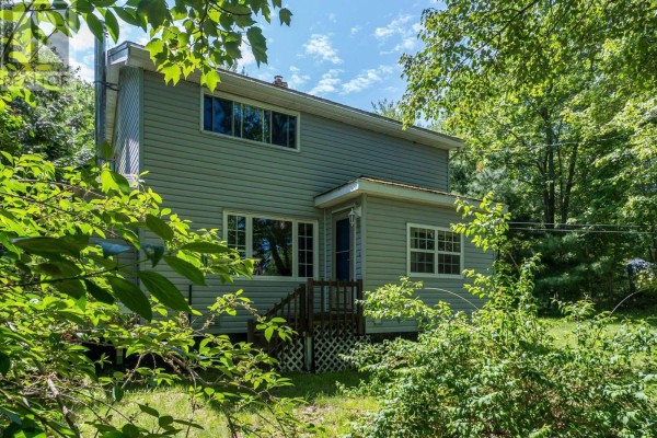 Aerial view of a light grey house with a wooden deck and surrounding green lawn and trees. - 161 Lakeview Road, Lakeview