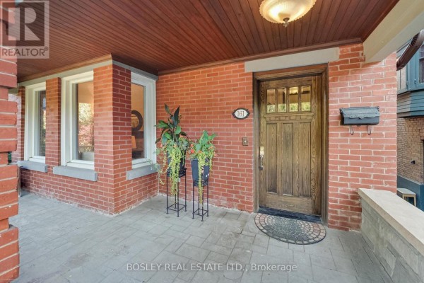 Covered front porch with red brick pillars, wooden door, and decorative plants. - 161 Westminster Avenue, Toronto
