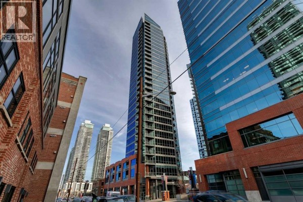 Exterior view of a tall, modern glass apartment building surrounded by other city structures. - 1610, 225 11 Avenue Se, Calgary