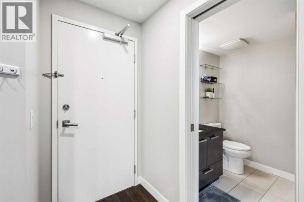 Apartment entryway with a white door and a view into a small bathroom with a toilet. - 1610, 225 11 Avenue Se, Calgary