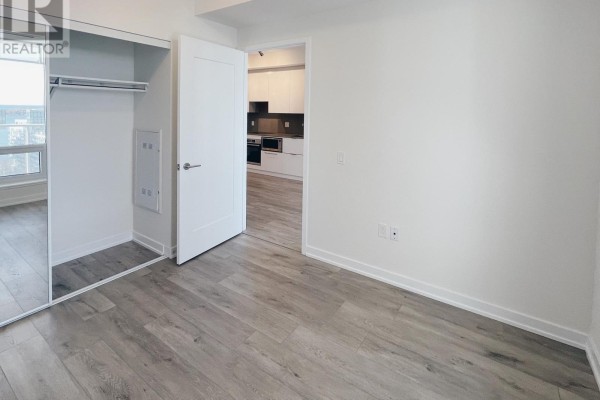 Bedroom with mirrored closet doors, light wood floors, and a doorway leading to the kitchen. - 1610 - 28 Freeland Street, Toronto