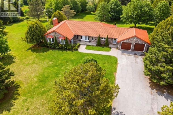 Aerial view of a large stone house with a red tile roof situated on a spacious, green lot. - 1610 Concession 7 Road, Hampton